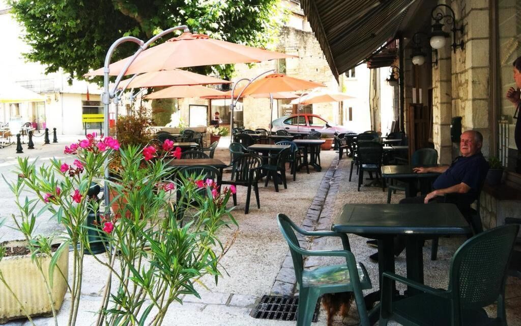Un café en plein air avec des tables, des chaises, des parasols et des plantes en pot.