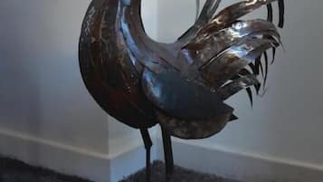 A metal rooster sculpture on a carpeted floor.