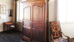 A room with a large wooden wardrobe, a small table, a chair, and a radiator. - Auberge du Puits (Souillac)