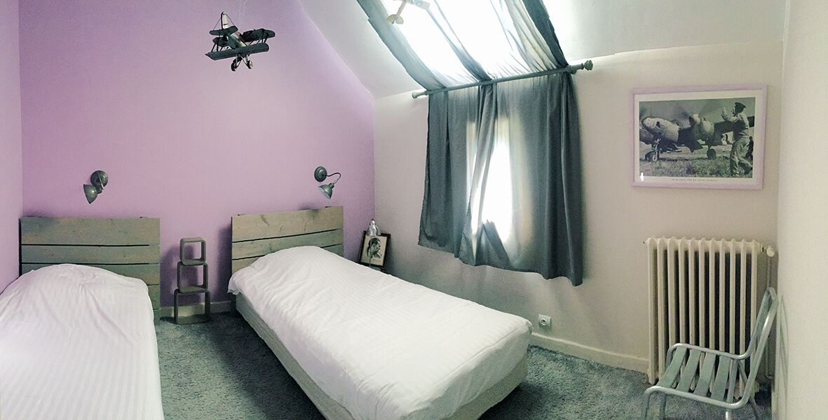 Een slaapkamer met twee enkele bedden, een radiator, een stoel en een raam met gordijnen.