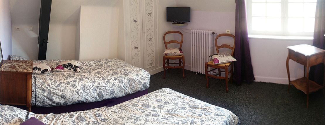 A bedroom with two beds, a wooden chair, a small table, a television, and a window with curtains.