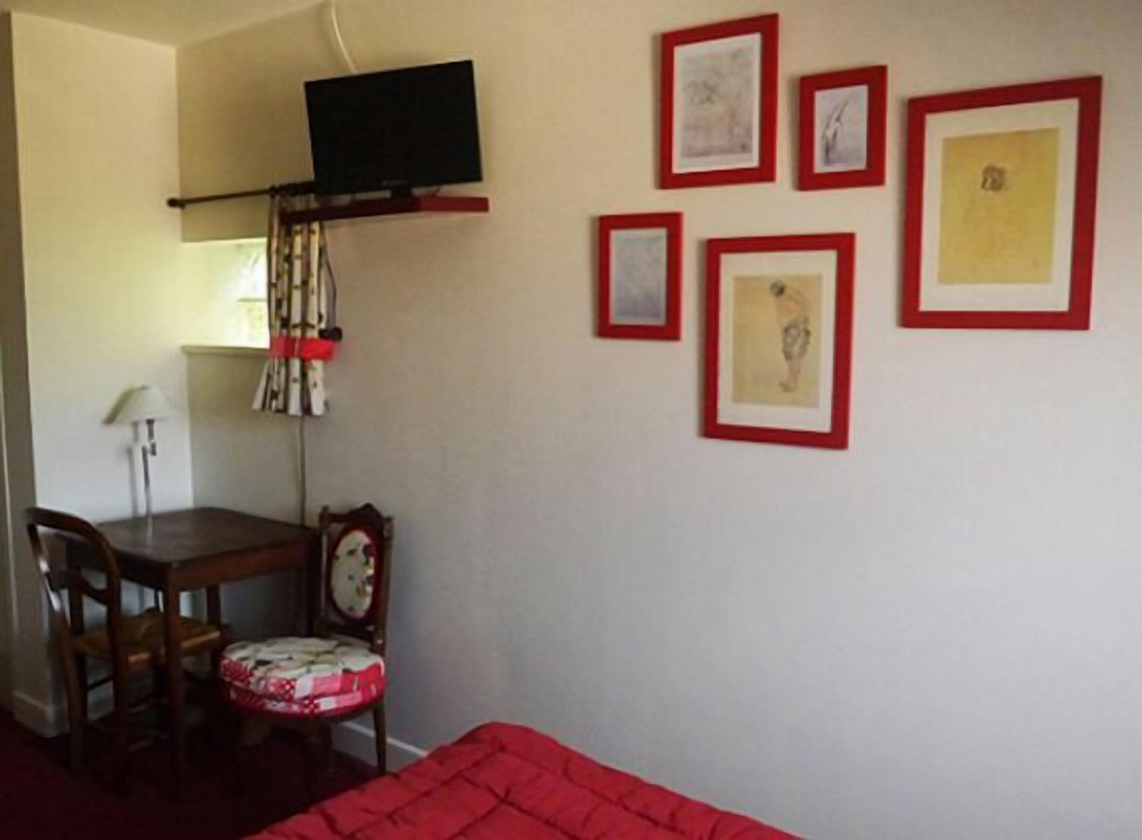 A room with a bed, a desk, and a chair. There are framed pictures on the wall.