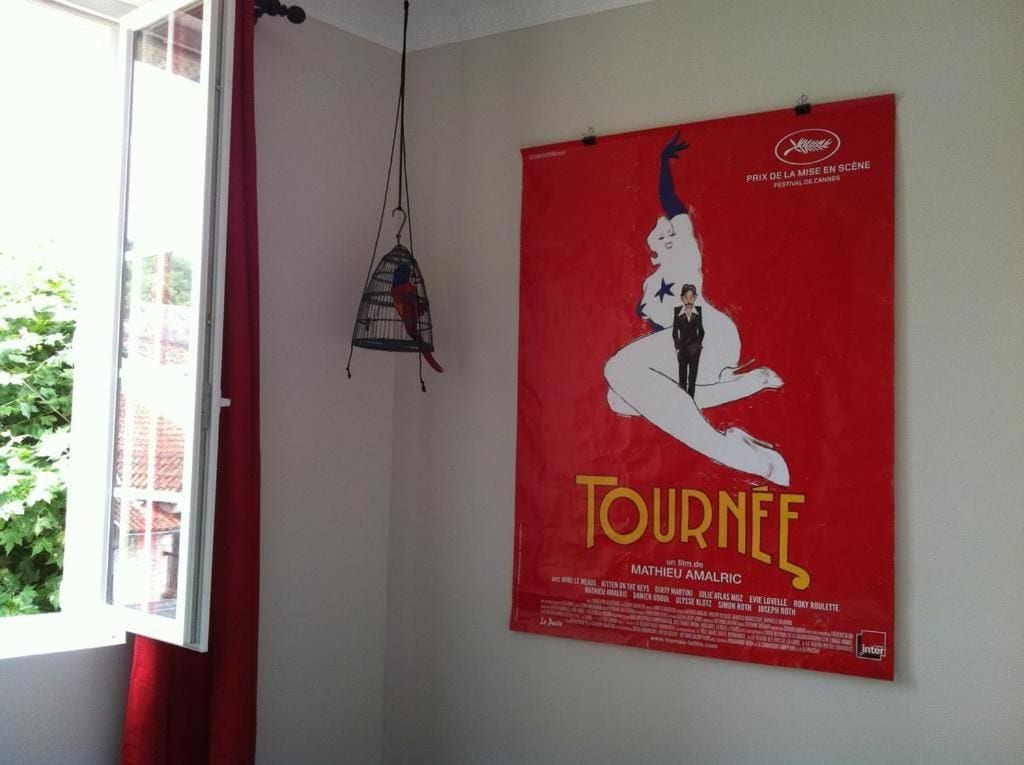 A room with a poster on the wall, a hanging light fixture, and a window with curtains.