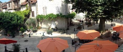 A courtyard with outdoor seating, surrounded by buildings with stone walls and shutters.