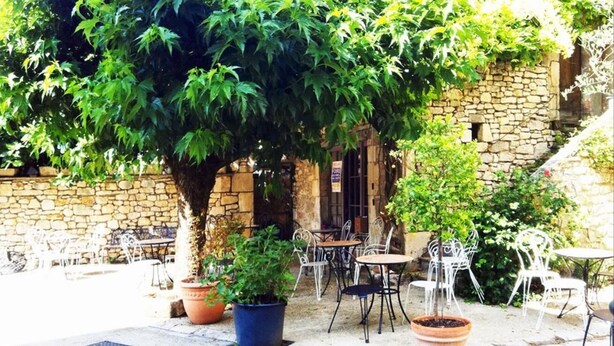 An outdoor café with stone walls, potted plants, and metal chairs. - Auberge du Puits (Souillac)
