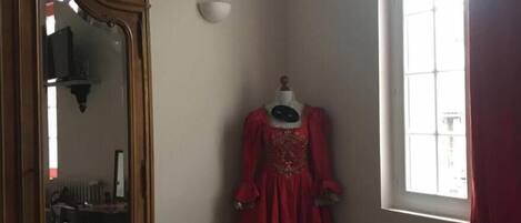 A room with a large mirror, a mannequin in a red dress, and a window with curtains.