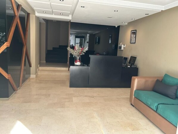 Un área de recepción con diseño moderno, que incluye un mostrador de recepción, un sofá y una escalera que conduce a los pisos superiores.