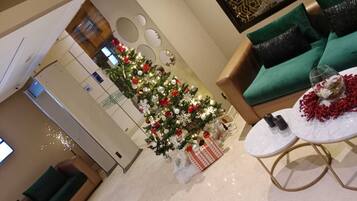 Una sala de estar moderna con un árbol de Navidad, sofás verdes y una mesita con una copa y flores.