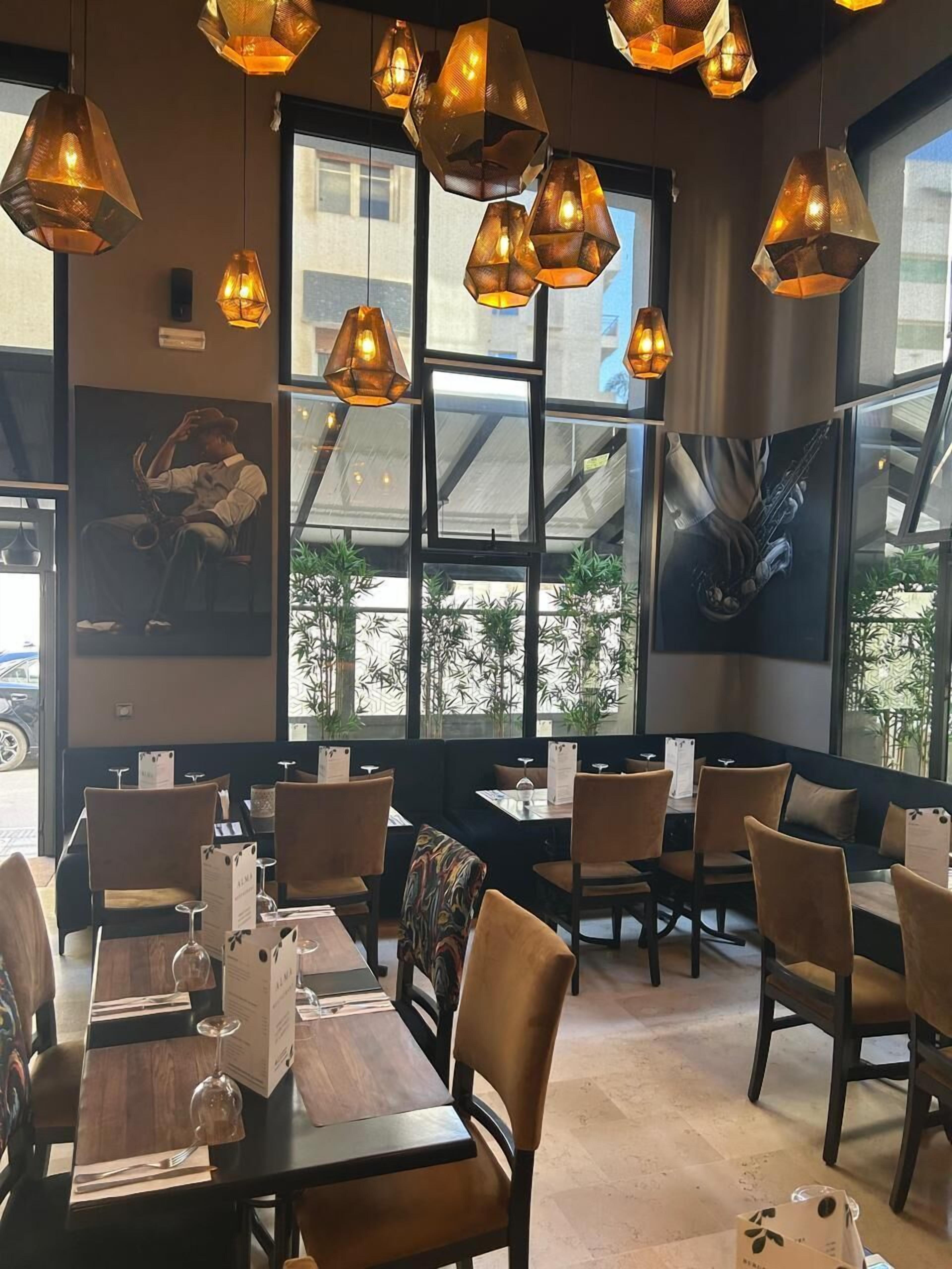 A restaurant interior with hexagonal pendant lights, large windows, and artwork on the walls.