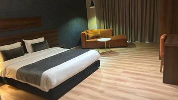 Moderni hotellihuone, jossa on suuri sänky, sohva, pieni pyöreä pöytä ja työpöytä.