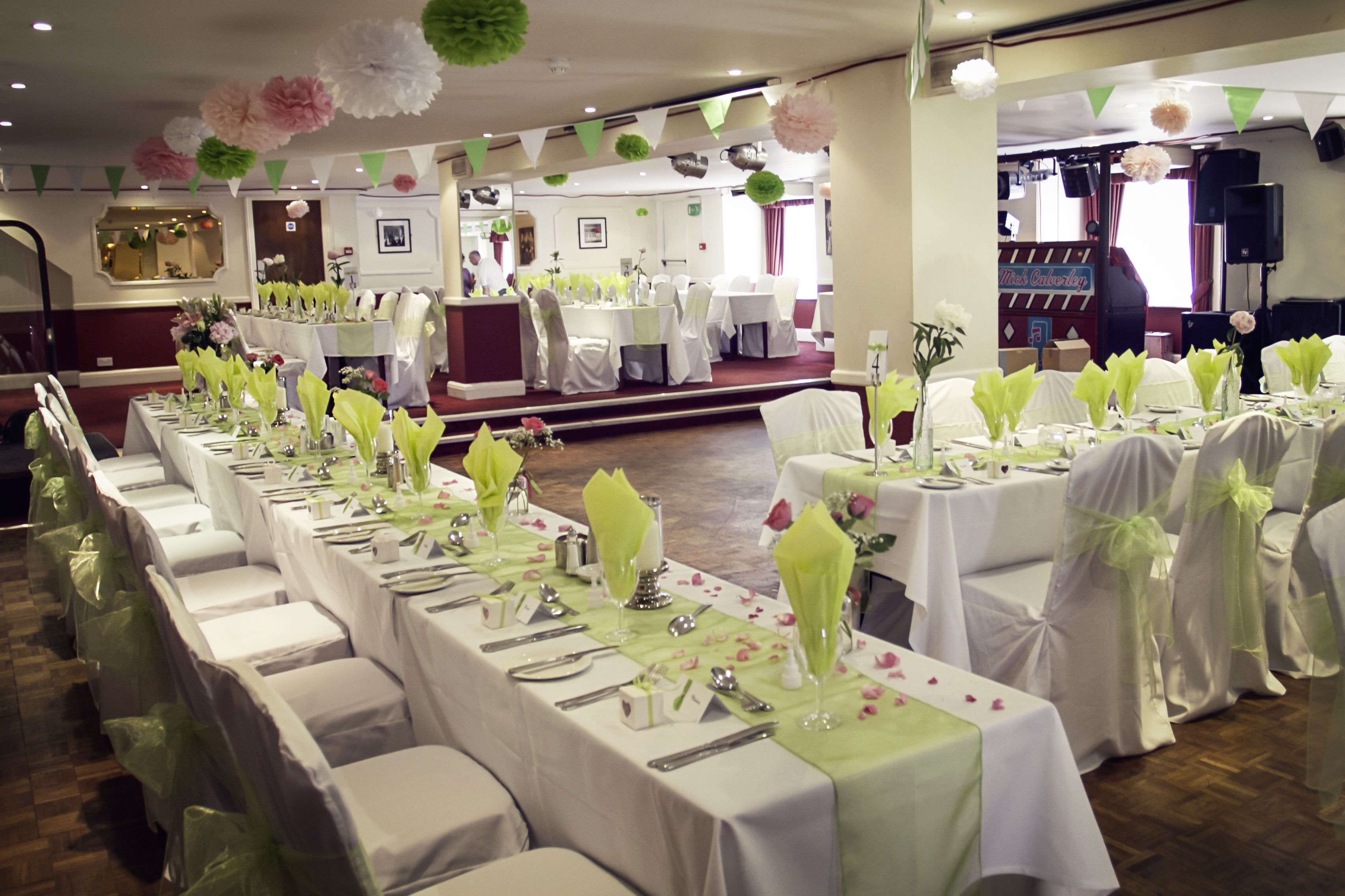 A banquet hall with long tables set for a formal event, featuring white tablecloths and green napkins.