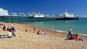 A pebbled beach with people sunbathing and walking. A pier extends into the water with buildings and a dome structure at the end. - Afton Hotel (Eastbourne)