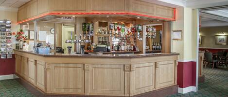 A bar area with a wooden counter, various bottles, and a patterned carpet.