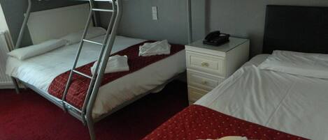 A hotel room with two beds, one with a bunk bed and the other with a single bed. There is a nightstand with a phone and a lamp.