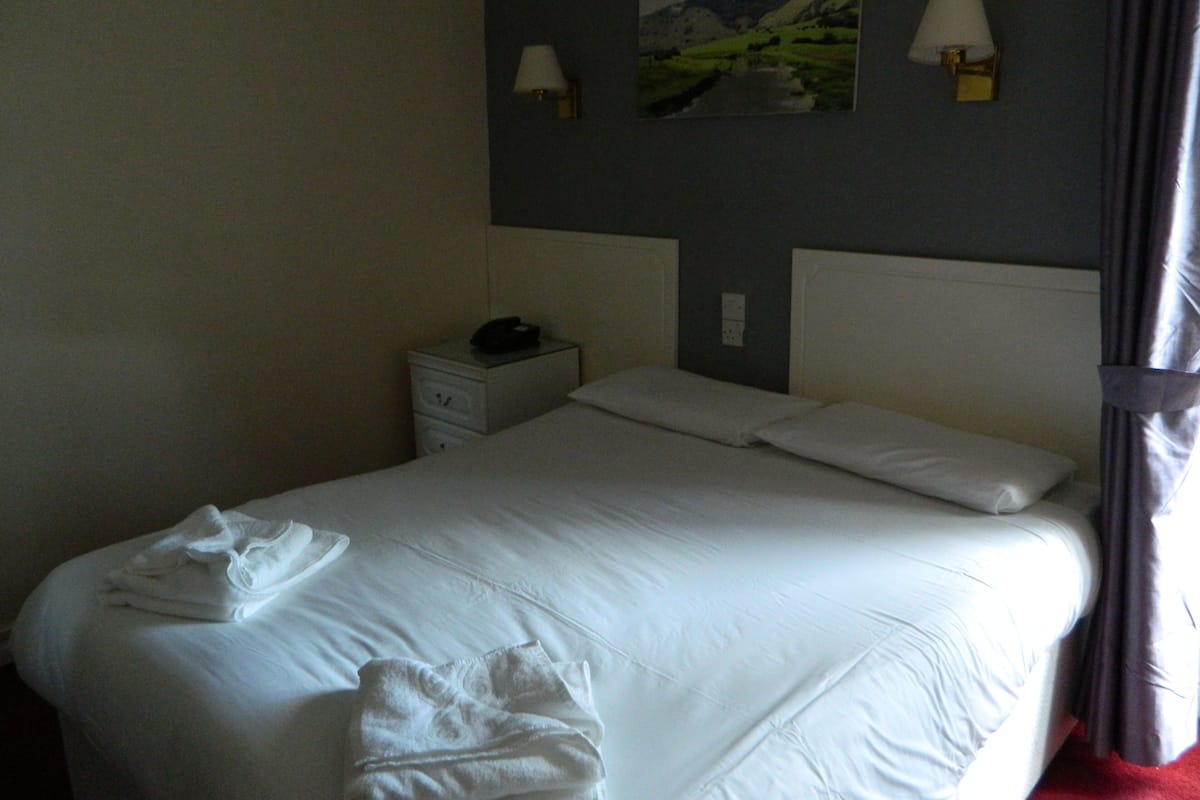A hotel room with a neatly made bed, a nightstand with a lamp, and a painting on the wall.