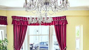 A room with a chandelier, red curtains, blue armchairs, a wooden coffee table, and a patterned carpet. - Afton Hotel (Eastbourne)