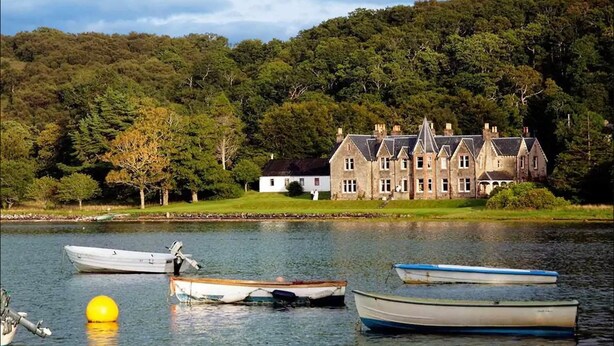 A large, historic house by a lake with several boats docked nearby. - Shieldaig Lodge Hotel (Gairloch)