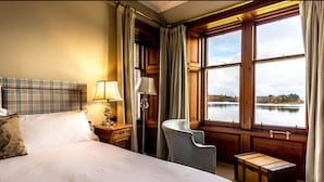 A hotel room with a large bed, a chair, a nightstand with a lamp, and a view of a lake through large windows. - Shieldaig Lodge Hotel (Gairloch)