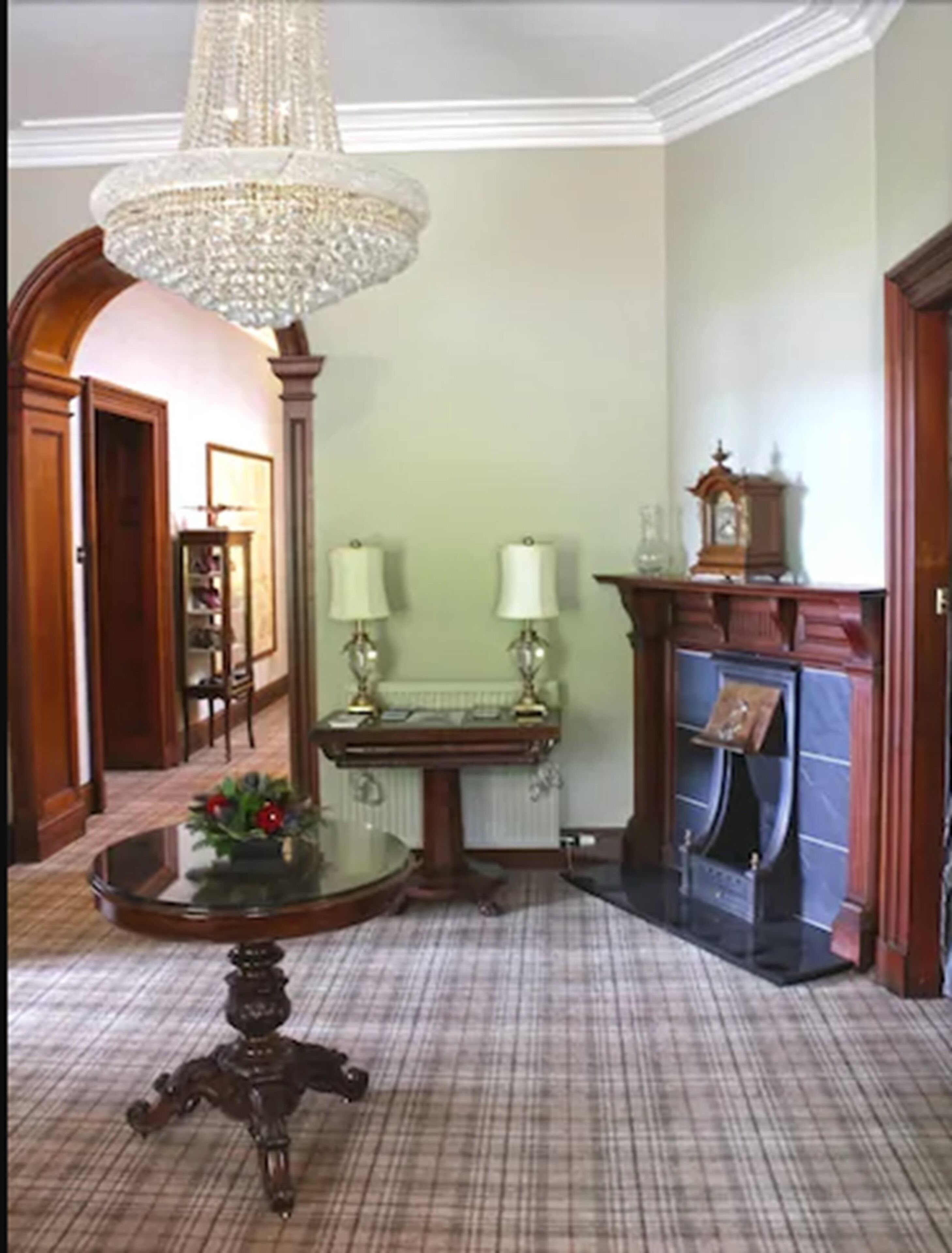 A room with a chandelier, a fireplace, a table with a vase, and a patterned carpet.
