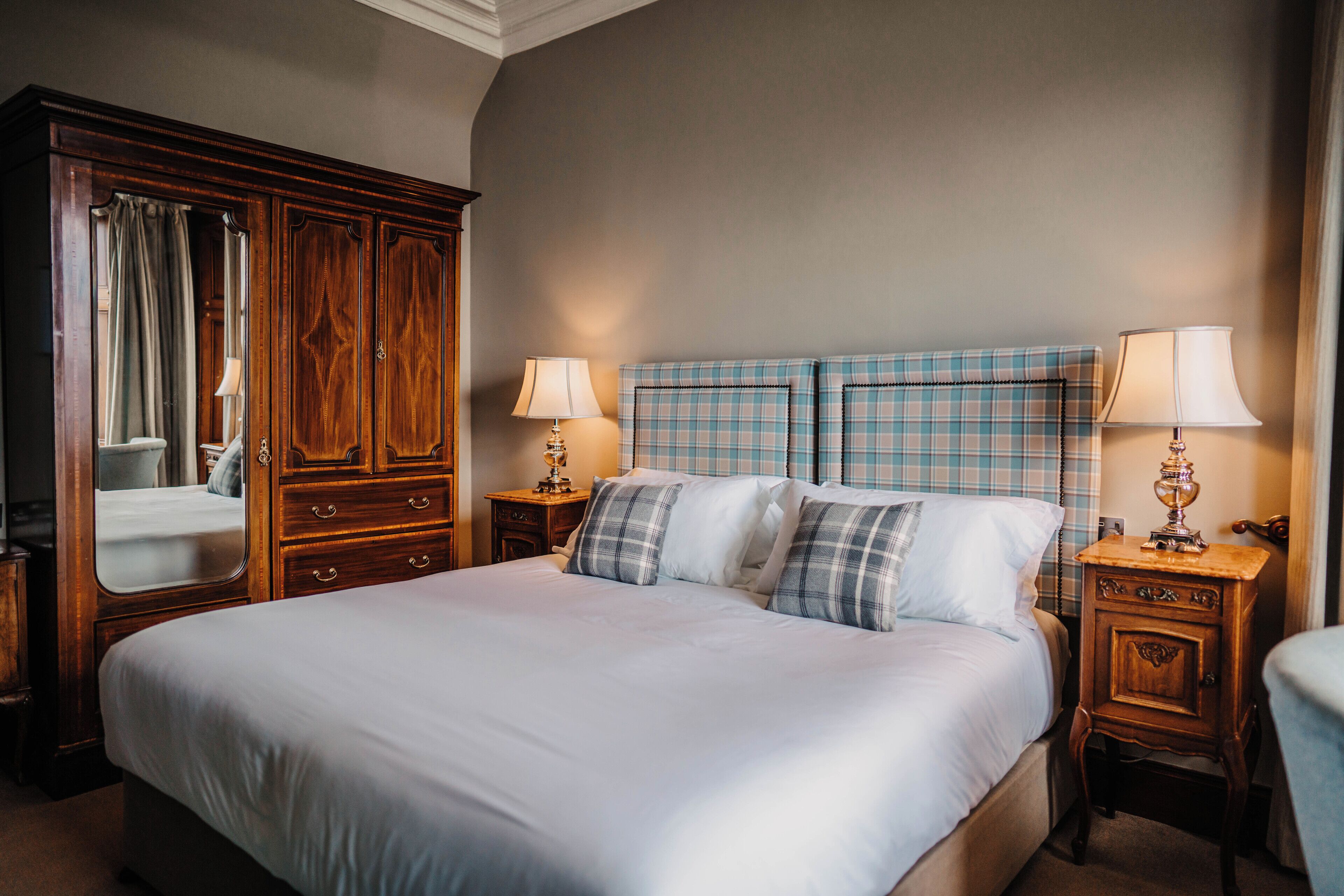 Une chambre à coucher bien rangée, avec un grand lit, une armoire en bois, deux tables de chevet avec des lampes et un miroir.