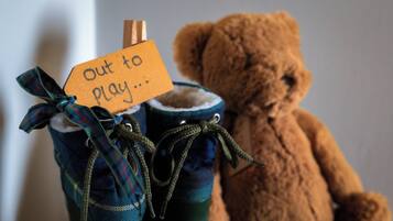 A teddy bear next to a pair of boots with a tag that reads "out to play...".