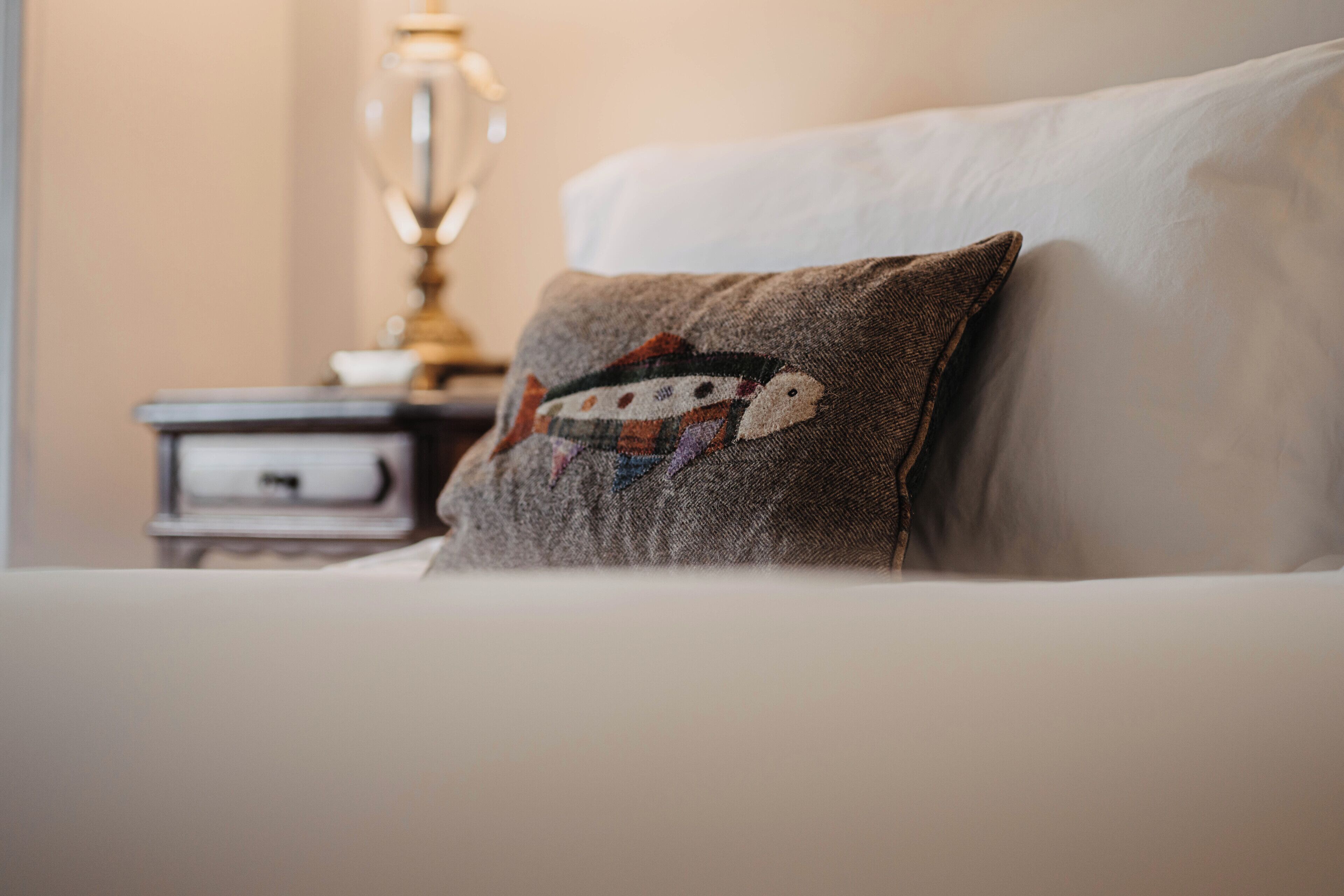 A neatly made bed with a pillow featuring a fish design.