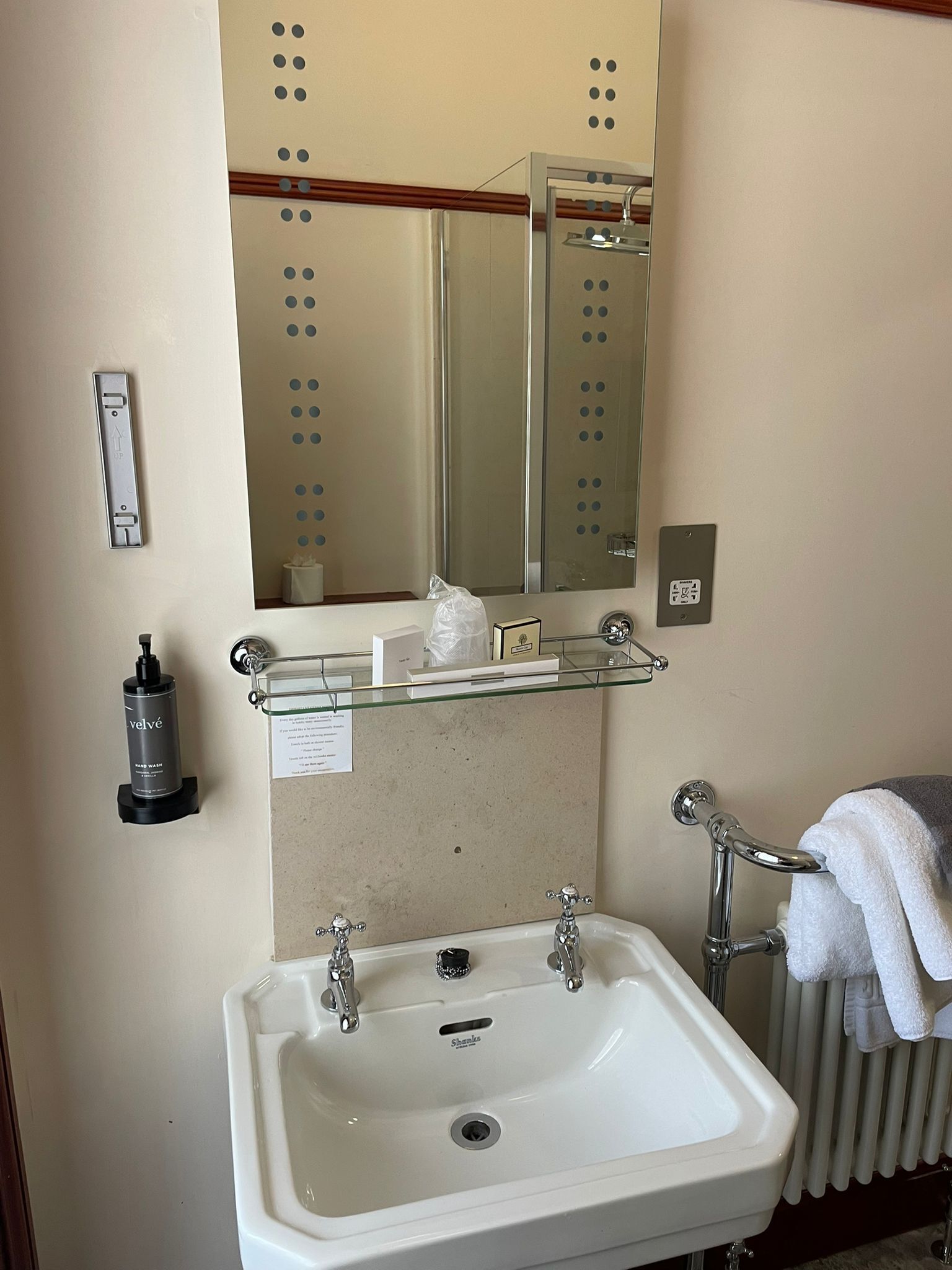 A bathroom with a white sink, a mirror, a towel rack, and a hand sanitizer dispenser.