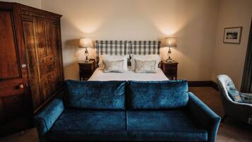 A bedroom with a bed, two bedside tables with lamps, a blue sofa, a wooden wardrobe, and a plaid armchair.