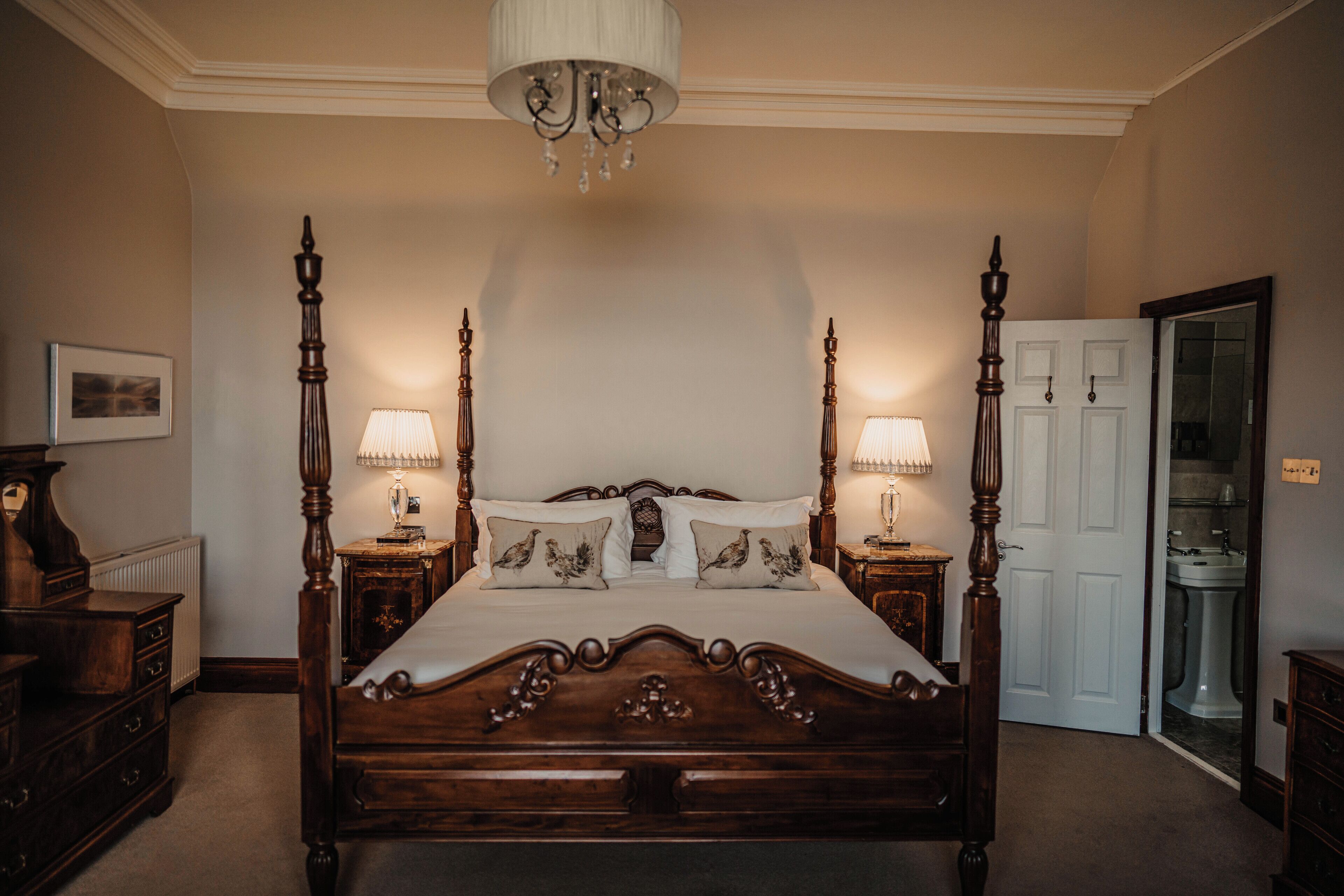 A four-poster bed with a wooden headboard, two bedside tables with lamps, and a white door in the background.