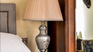 Una cama con una colcha blanca, una lámpara decorativa con pantalla color beige y una mesita de noche de madera.