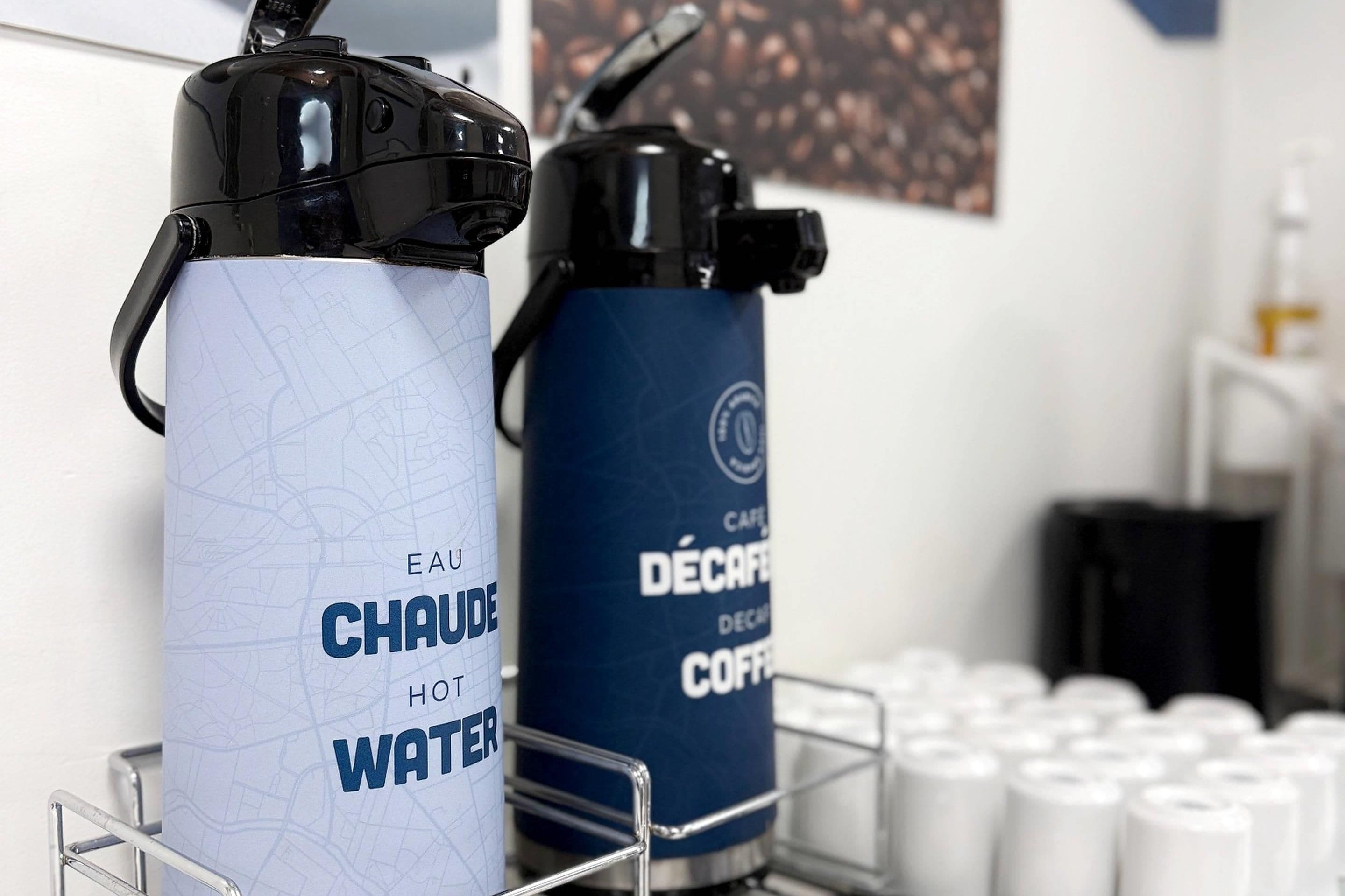 Two water bottles on a metal rack, one labeled 'EAU CHAUDE HOT WATER' and the other 'CAFE DÉCafé Deco Coffee'.