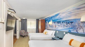 Habitación de hotel con dos camas, un televisor, una silla y un mural de un paisaje nevado.