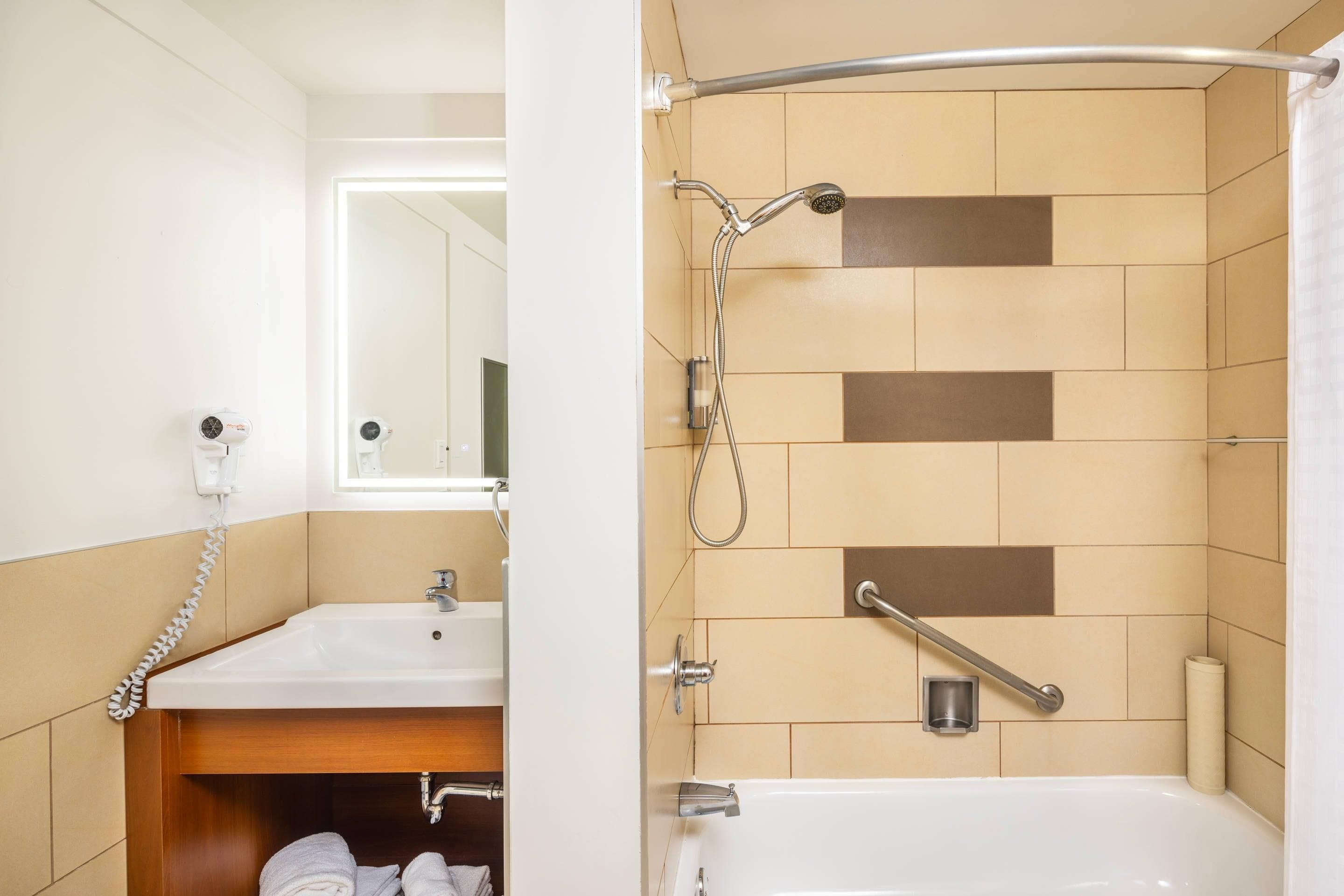 A bathroom with a shower, a sink, a mirror, and a towel rack.