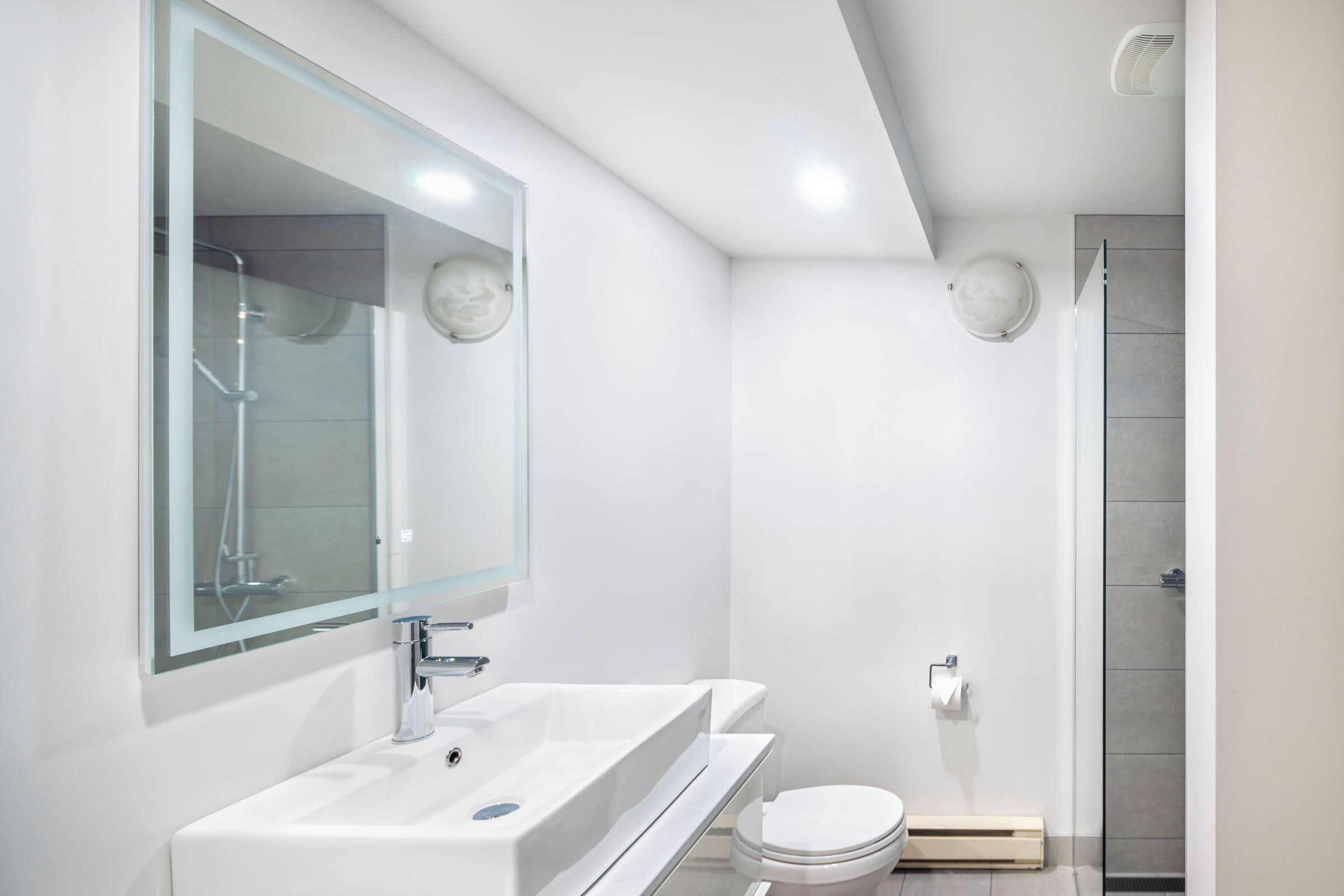 A modern bathroom with a large mirror, white sink, and toilet.