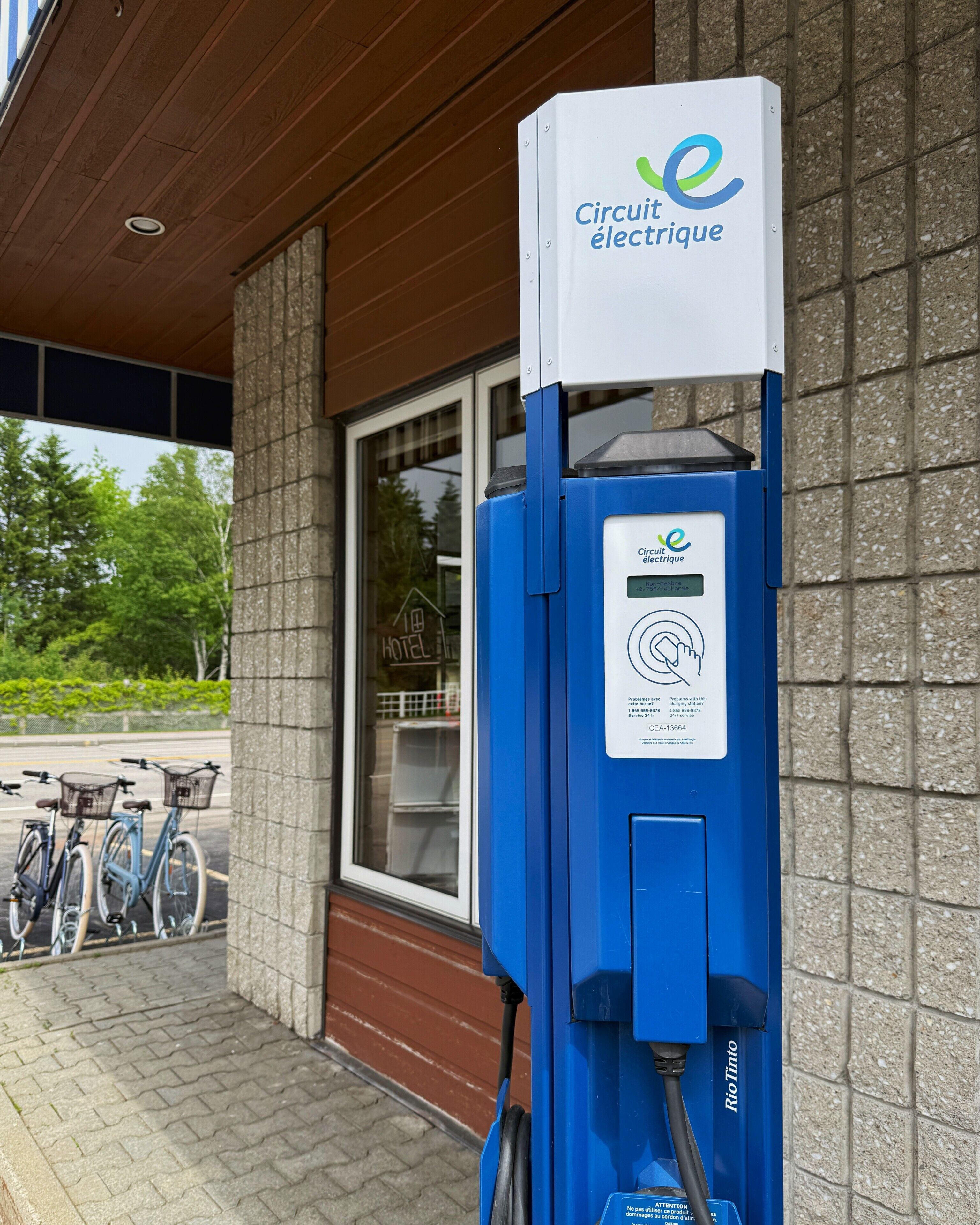 En laddstation för elfordon med en skylt som visar texten ”Circuit électrique” utanför en byggnad där ett fönster visar en skylt med texten ”HOTEL”.