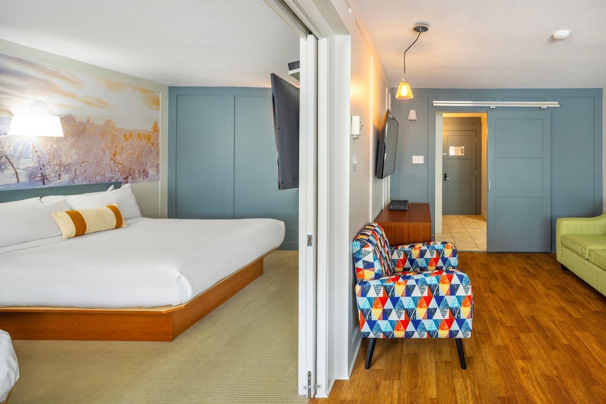 Une chambre d’hôtel avec un lit, une chaise colorée, un canapé vert et un tableau au mur.