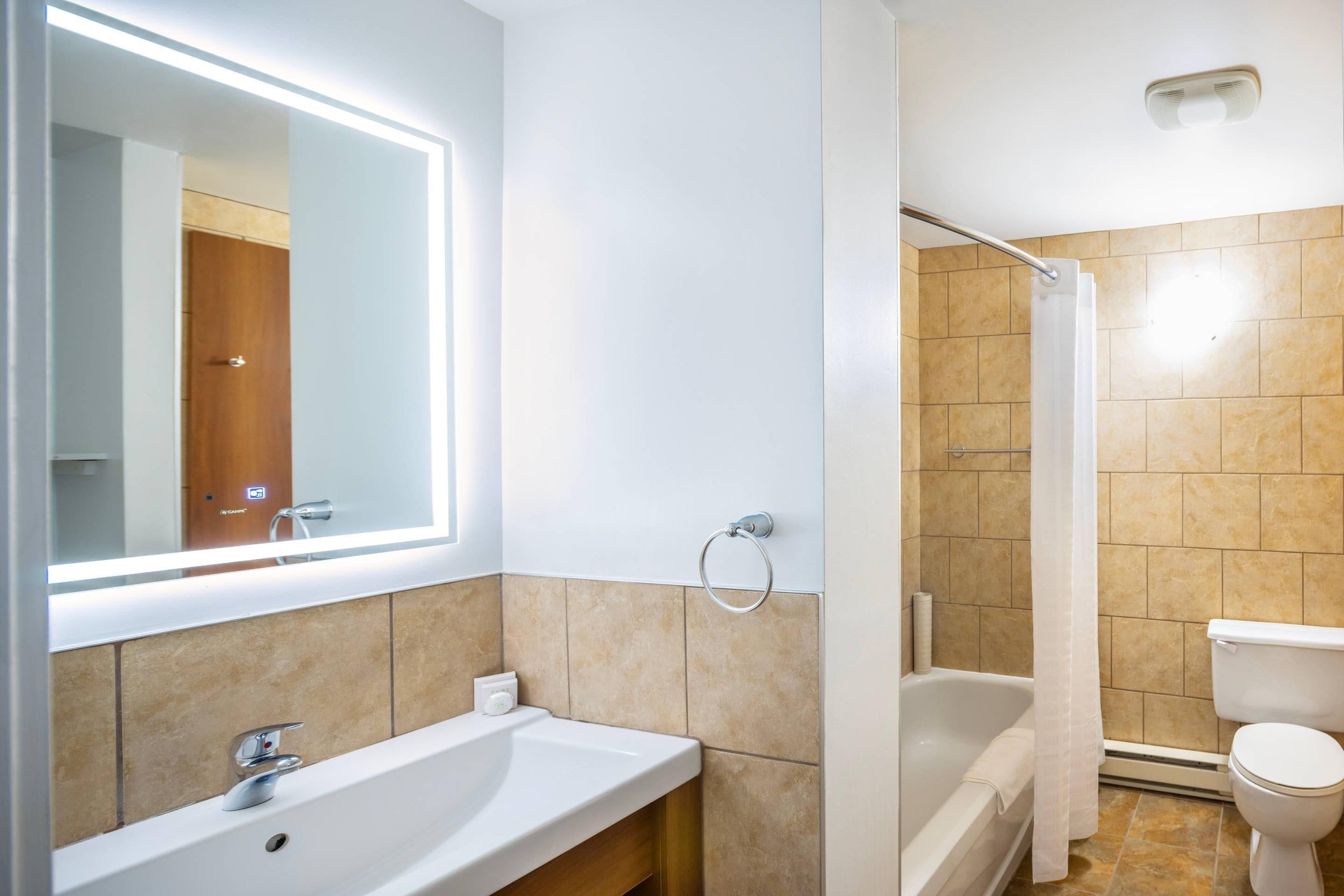 Un baño moderno con un espejo grande, un lavabo, una ducha y un inodoro.