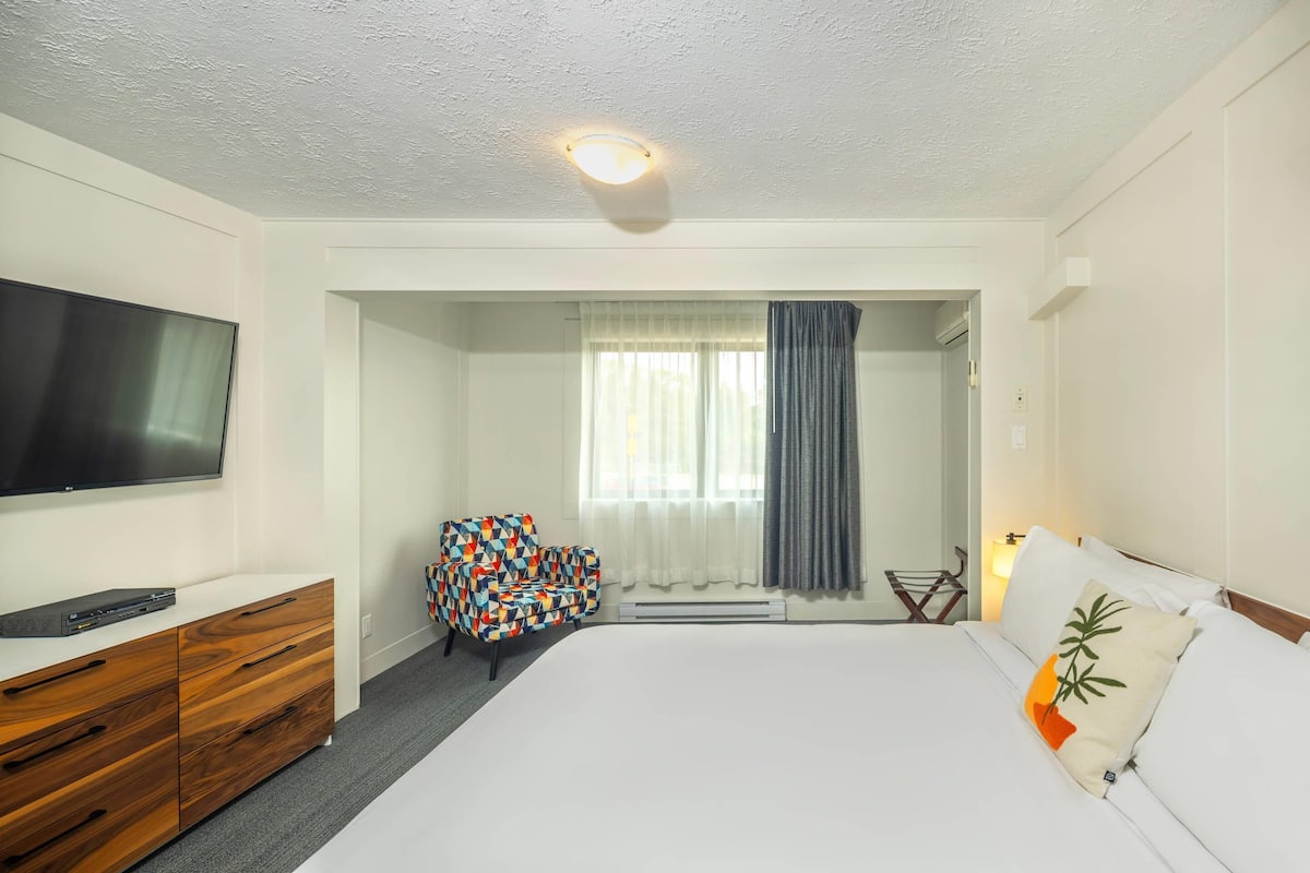 Une chambre d’hôtel équipée d’un lit, d’une télévision, d’une commode, d’une chaise et d’un espace douche.
