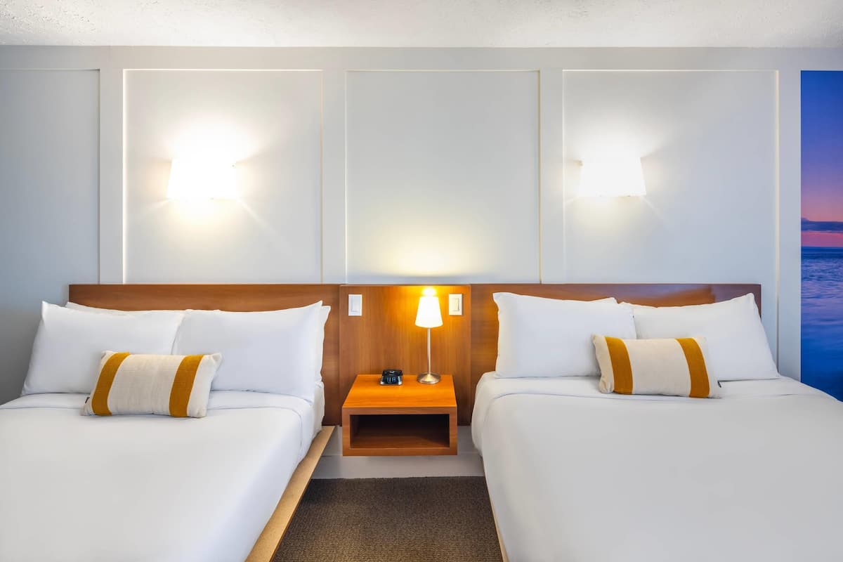 Une chambre d’hôtel avec deux lits, une table de chevet avec une lampe et des lampes fixées au mur.