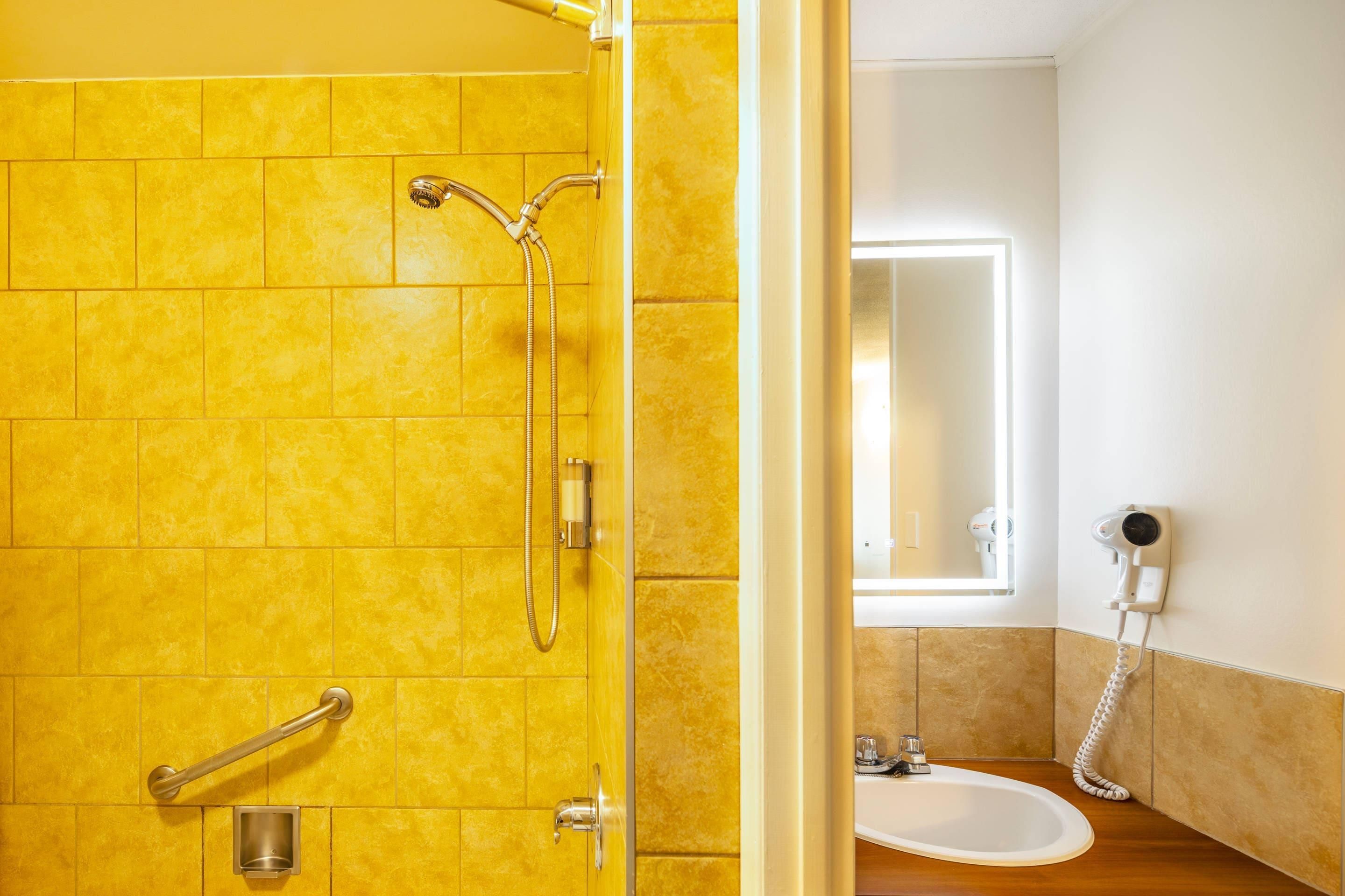 Un baño con azulejos amarillos, una ducha, un secamanos y un lavamanos.