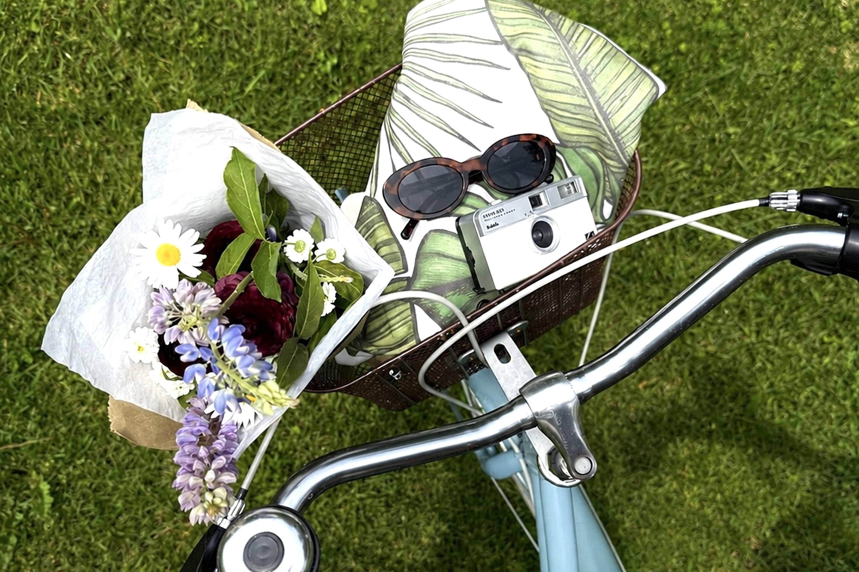 A bicycle with a basket containing a bouquet of flowers, sunglasses, and a cassette tape.