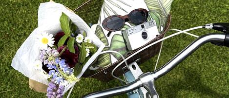 A bicycle with a basket containing a bouquet of flowers, sunglasses, and a cassette tape.