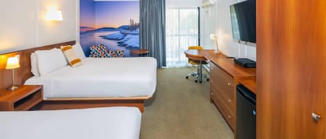 Habitación de hotel con dos camas, un escritorio, un televisor y un amplio ventanal con vistas panorámicas.
