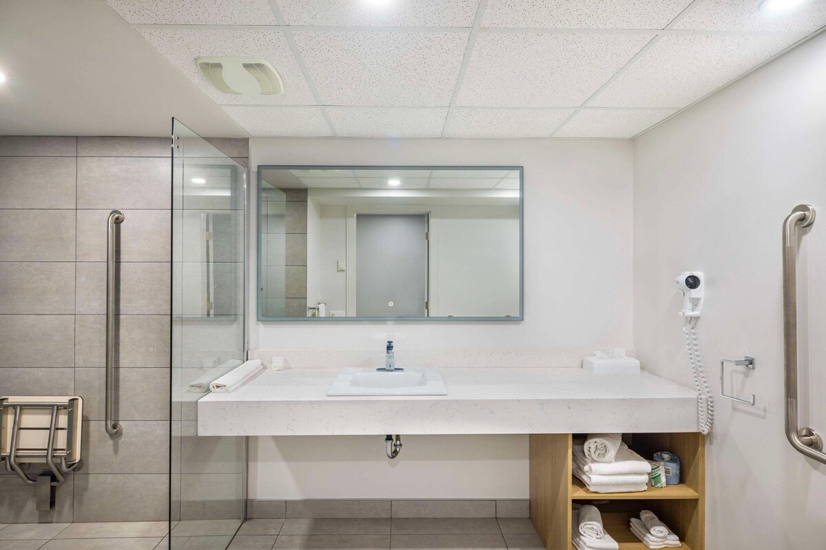 Een moderne badkamer met een douchecabine van glas, een wit wastafelmeubel met spiegel erboven en een handdoekrek.