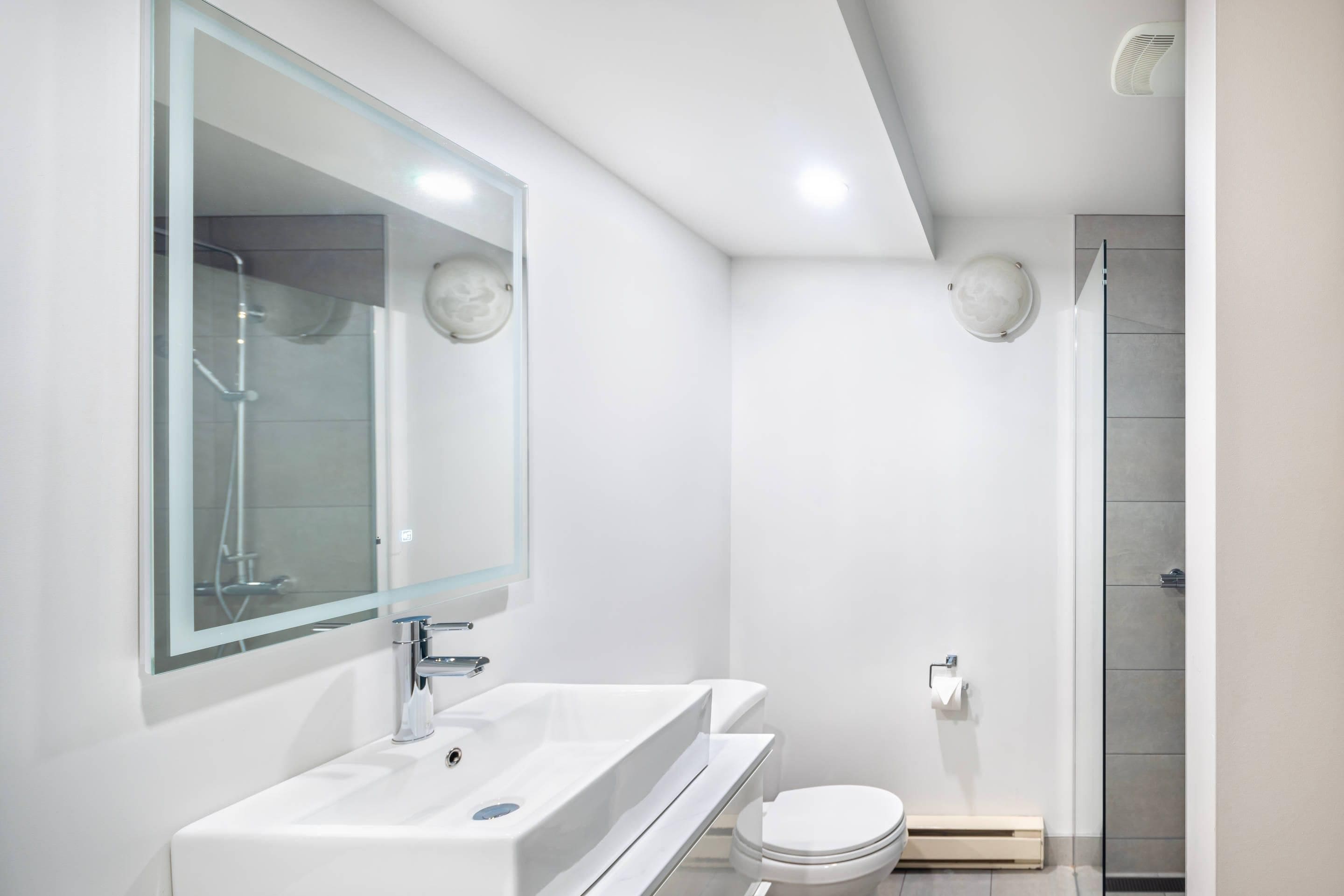 A modern bathroom with a large mirror, a sink, a toilet, and a shower.