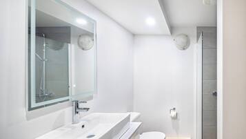 A modern bathroom with a large mirror, a sink, a toilet, and a shower.