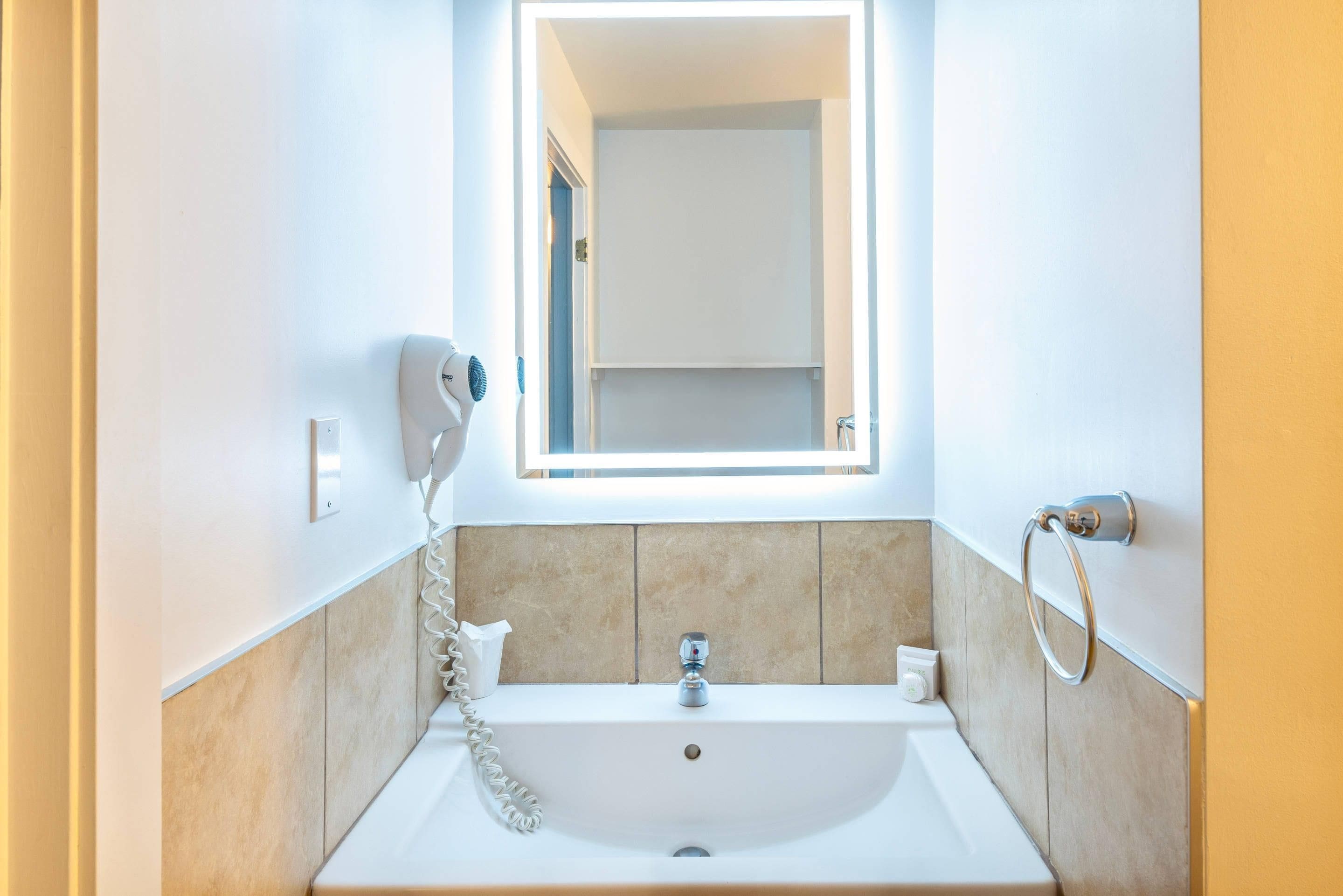 Une salle de bain avec un lavabo blanc, un miroir, un porte-serviettes et un sèche-cheveux.