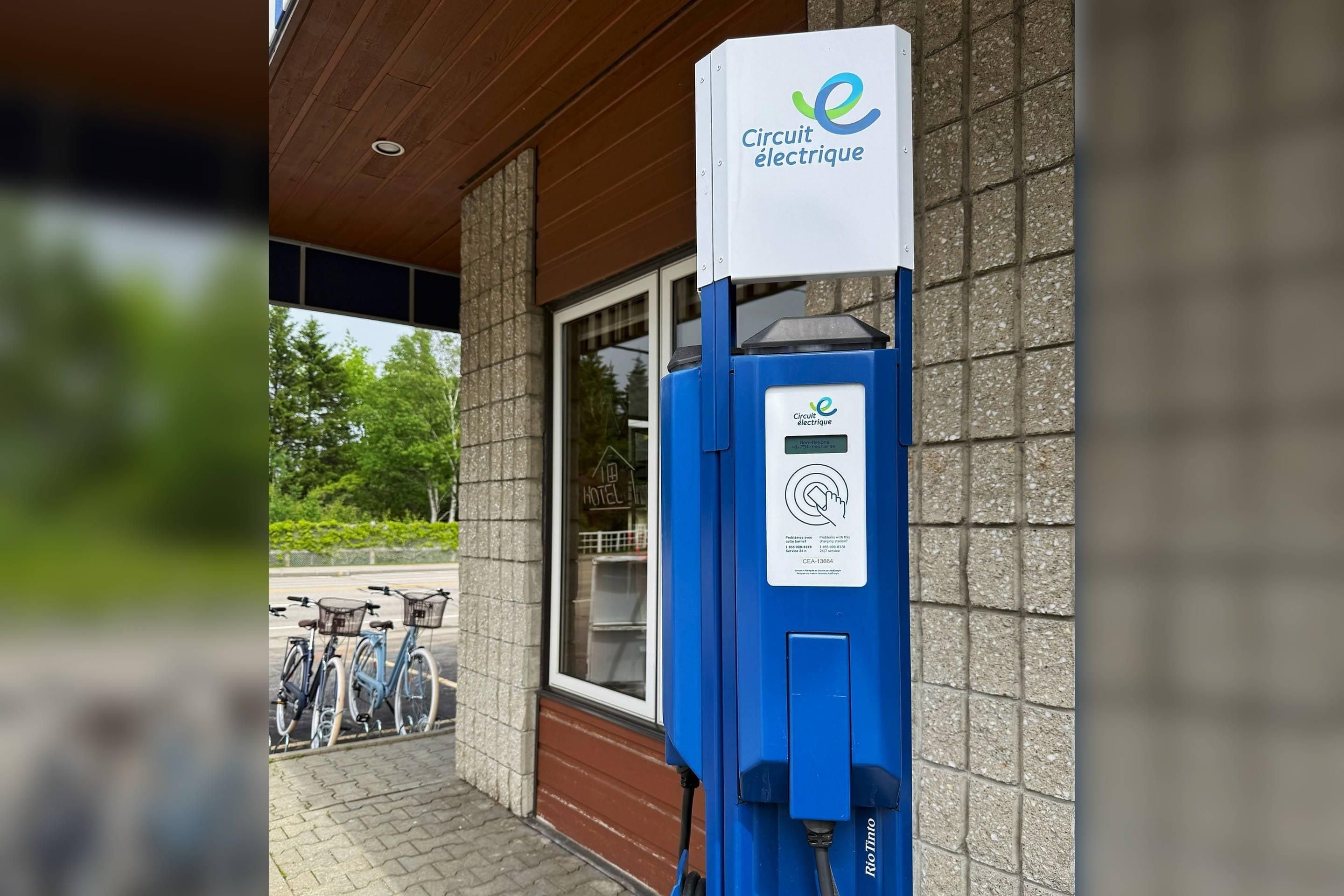 Una estación de carga eléctrica con un letrero que dice 'Circuit électrique' frente a un edificio con una ventana y una puerta.