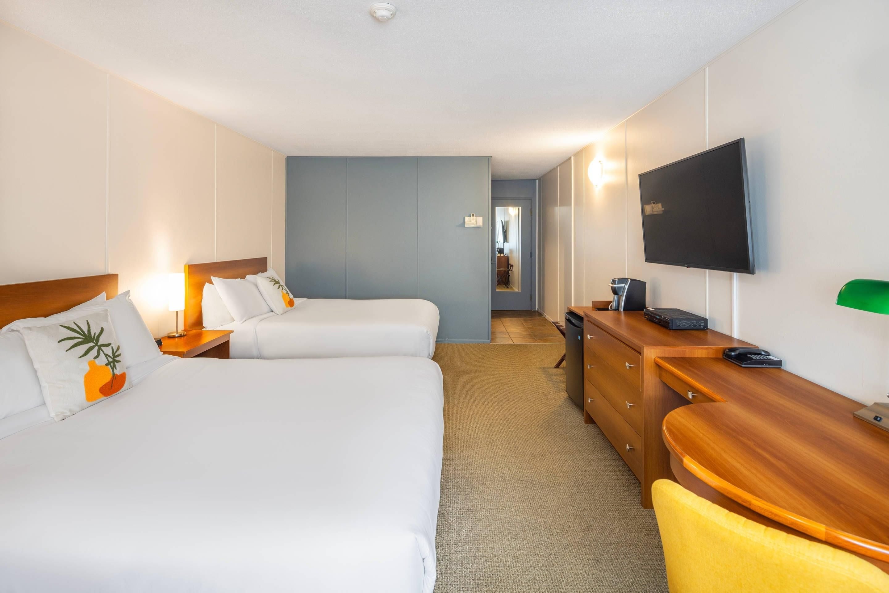 A hotel room with two beds, a desk, a chair, a TV, and a mirror.