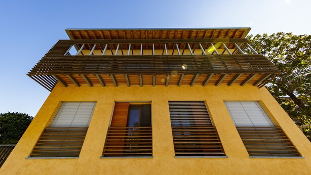 Een geel gebouw met veel ramen en een houten balkon.